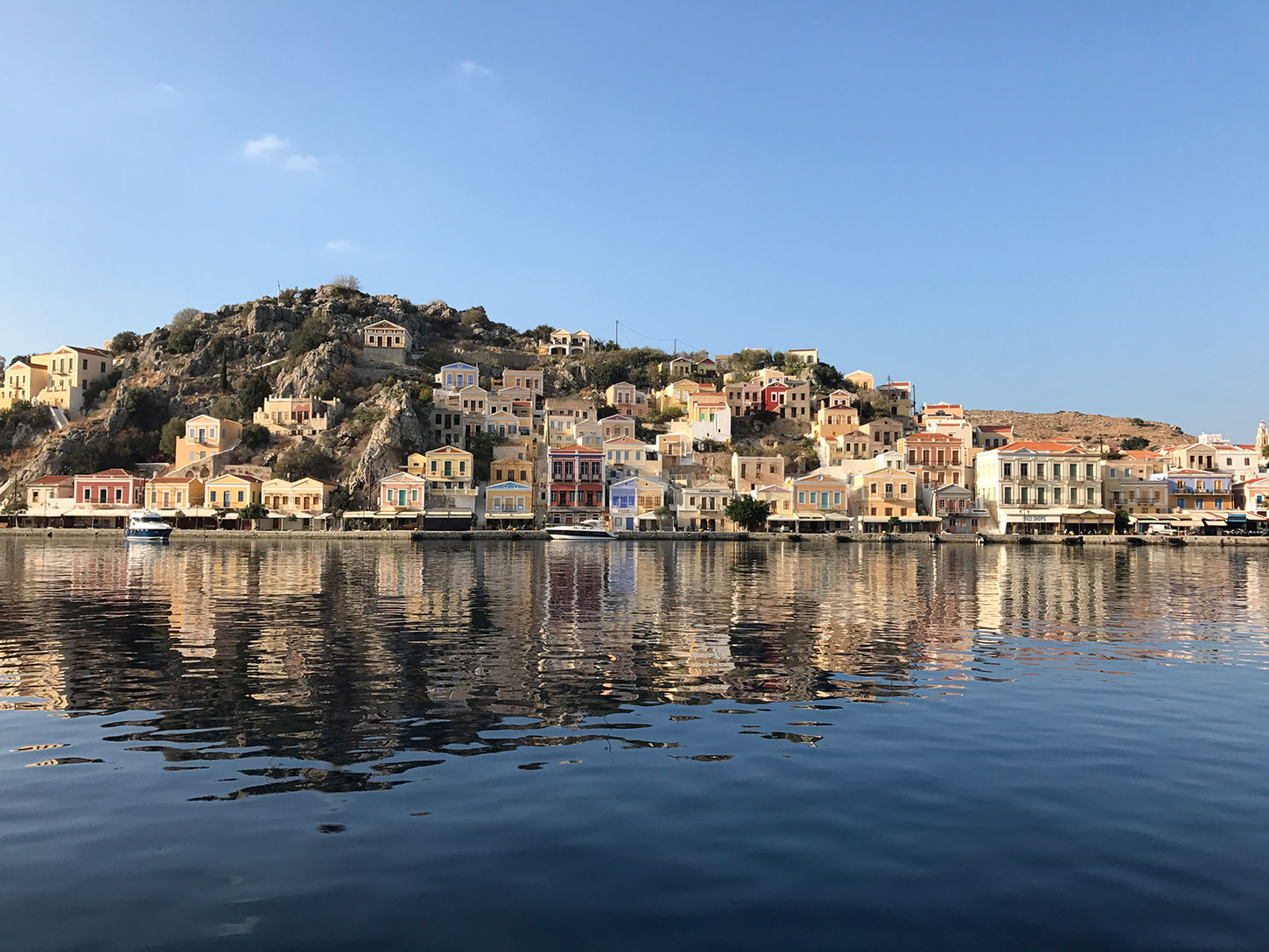 Symi houses around the port. The sea is calm and the sky is clear.